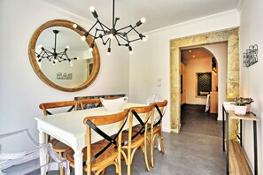 A dining area with a white table, wooden chairs, a modern chandelier, and a large mirror. - Portas do Sol Terrace –pure charm in Alfama (A/C) (Lisbon)