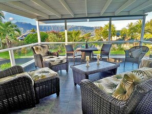 A covered outdoor seating area with wicker furniture and a view of mountains and greenery.