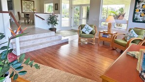 A spacious living area with a wooden floor, a staircase leading to a balcony, and a dining area with wicker furniture. - Ramatici Ohana Hale, Fabulous updated home with shared pool and tennis court. (Princeville)