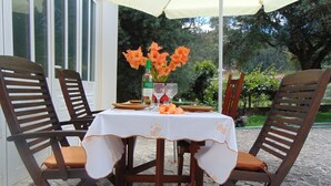 Un área de comedor al aire libre con una mesa dispuesta para dos personas, rodeada de sillas de madera con cojines.