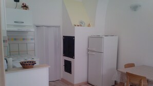 Una cocina pequeña y limpia con refrigerador, una mesa de comedor con sillas y piso de madera.