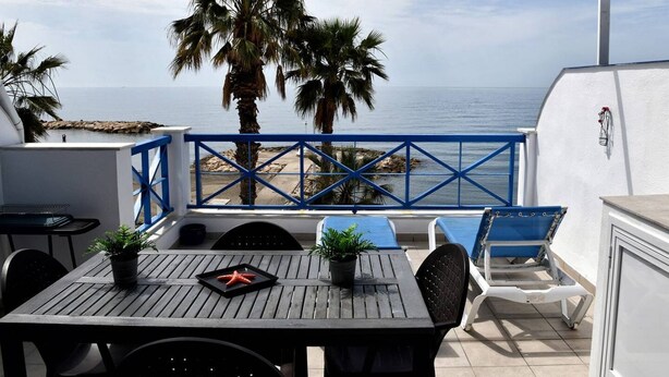 Un patio al aire libre con mesa, sillas y vista al mar.