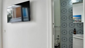 Un baño moderno con un salpicadero de azulejos estampados, un televisor montado y una pequeña estantería con una fotografía.