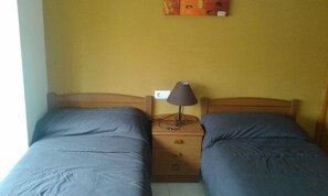 A twin room with two beds, a nightstand with a lamp, and a wall socket.