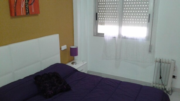 Un dormitorio con cama, mesita de noche, lámpara y ventana con persianas.