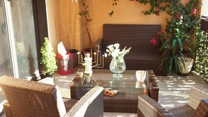 A sunlit room with wicker furniture, a glass coffee table, and potted plants.