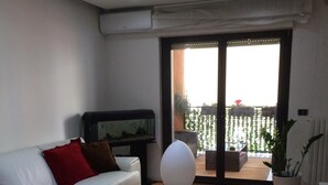 A living room with a white sofa, a coffee table with magazines, a fish tank, and a balcony with a view.
