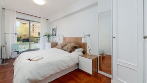 Ein modernes Hotelzimmer mit einem großen Bett, Nachttischen, einem Spiegel und einem Balkon mit Blick auf Gebäude und Grünflächen.