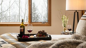 Una habitación acogedora con una cama, una ventana con vistas a árboles, una bandeja con una botella de vino, copas y una fuente de uvas.