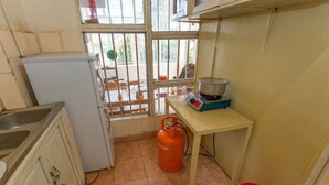 A compact kitchen with a refrigerator, gas cylinder, and a small table with a pot. - Golf Eden Guest House (Kigali)