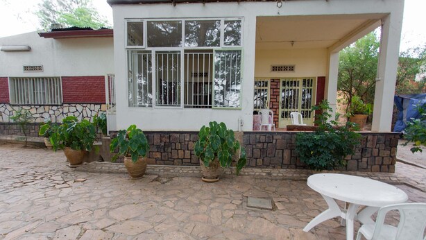 A building with a stone-paved patio, potted plants, and a white plastic table and chair. - Golf Eden Guest House (Kigali)