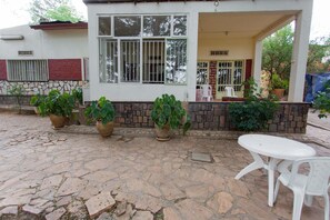 A building with a stone-paved patio, potted plants, and a white plastic table and chair. - Golf Eden Guest House (Kigali)