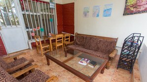A living room with a patterned sofa, wooden chairs, a glass-top coffee table, and a metal rack. - Golf Eden Guest House (Kigali)