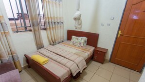 A bedroom with a bed, a nightstand, a chair, and a wooden door. - Medi Motel (Kigali)