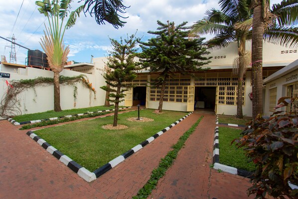 Un patio con sendero empedrado, palmeras y un edificio con entrada porticada.