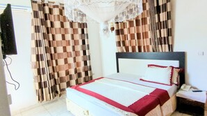 A bedroom with a bed, curtains, a nightstand, and a telephone. - Silver Hotel (Kigali)