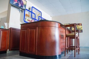 A reception desk with a curved design, a blue-framed display of liquor bottles, and a wooden chair with a cushion.