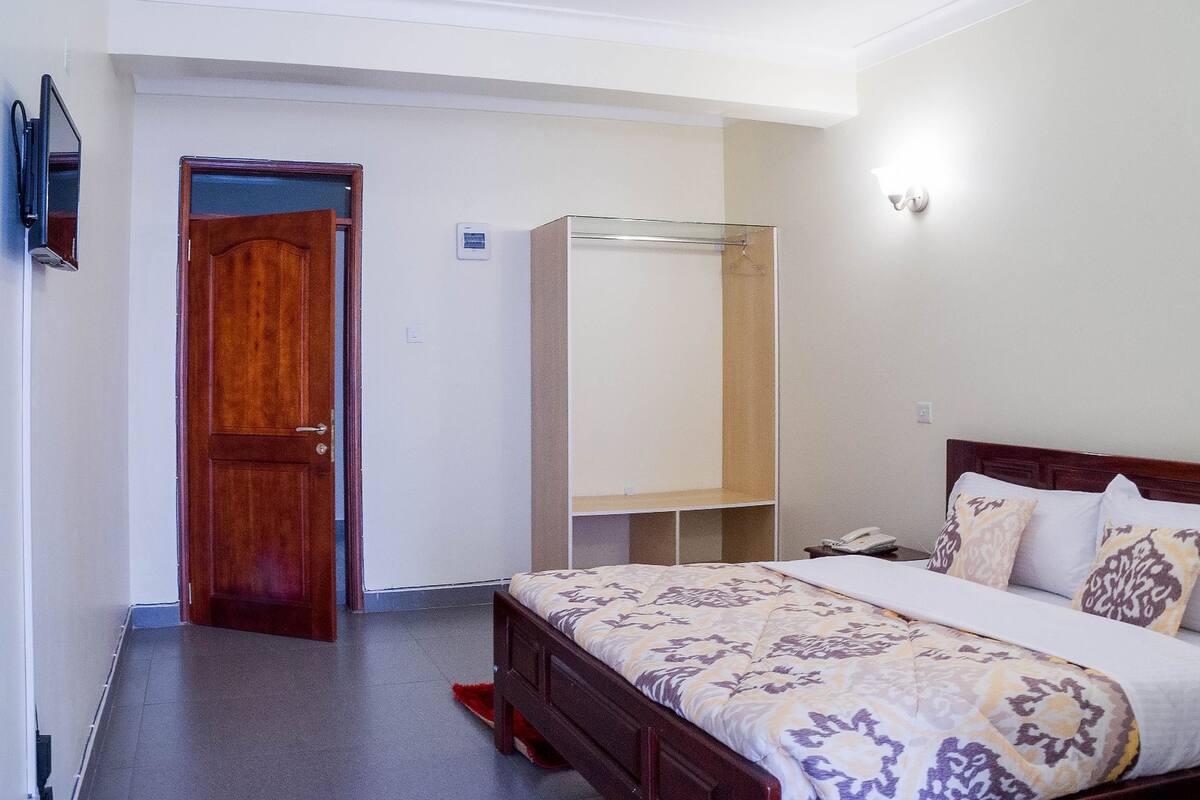 A bedroom with a wooden door, a bed with patterned bedding, a bedside table, and a wardrobe.