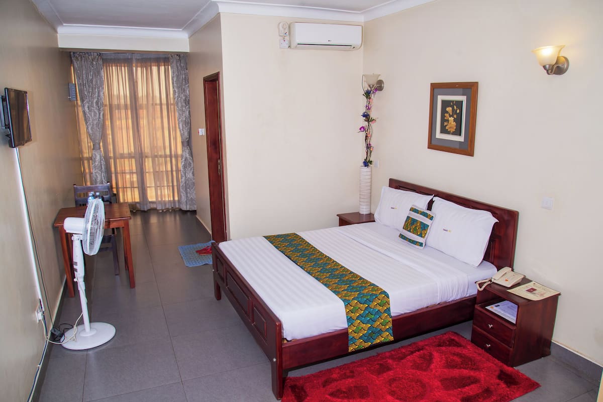 A hotel room with a bed, bedside table, and a standing fan.