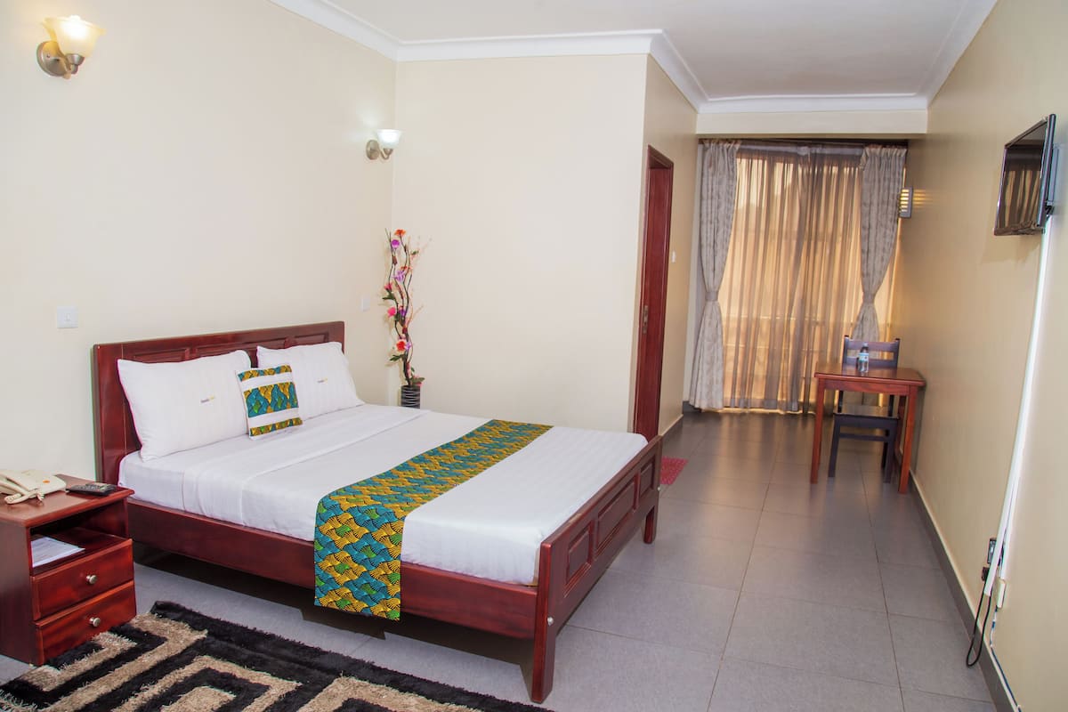 A neatly arranged hotel room with a wooden bed, a bedside table, a nightstand, a small table, and a chair.