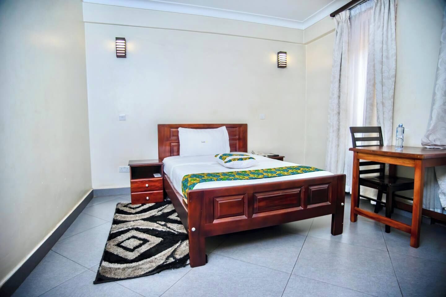 A neatly arranged bedroom with a wooden bed, a bedside table, a chair, and a small desk.