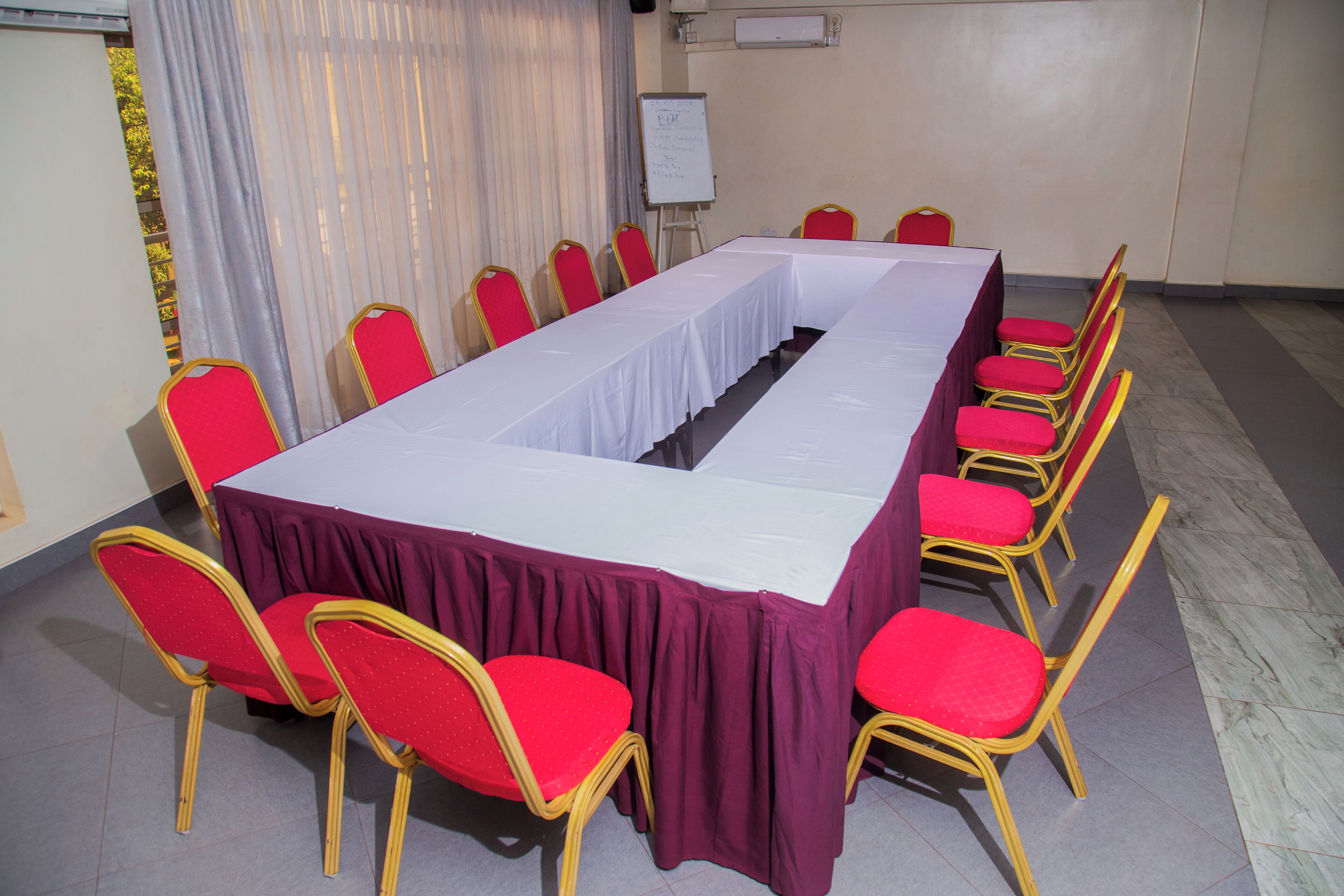 Un salón de conferencias con una larga mesa, sillas rojas y una pizarra.