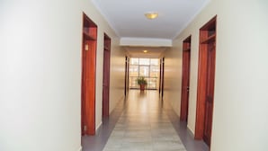 A hallway with wooden doors, a tiled floor, and a ceiling light. - Kenendia Hotel (Kampala)