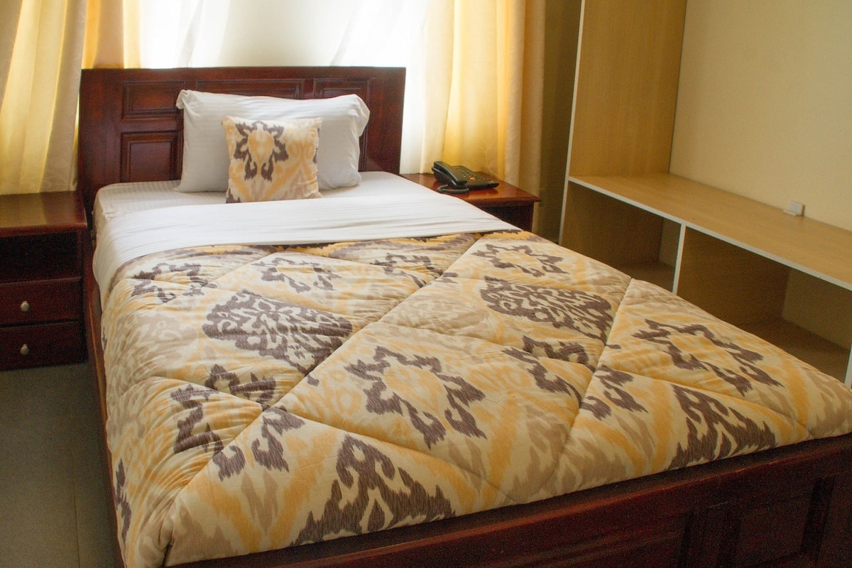 A neatly made bed with a patterned bedspread, a bedside telephone, and a wooden nightstand.