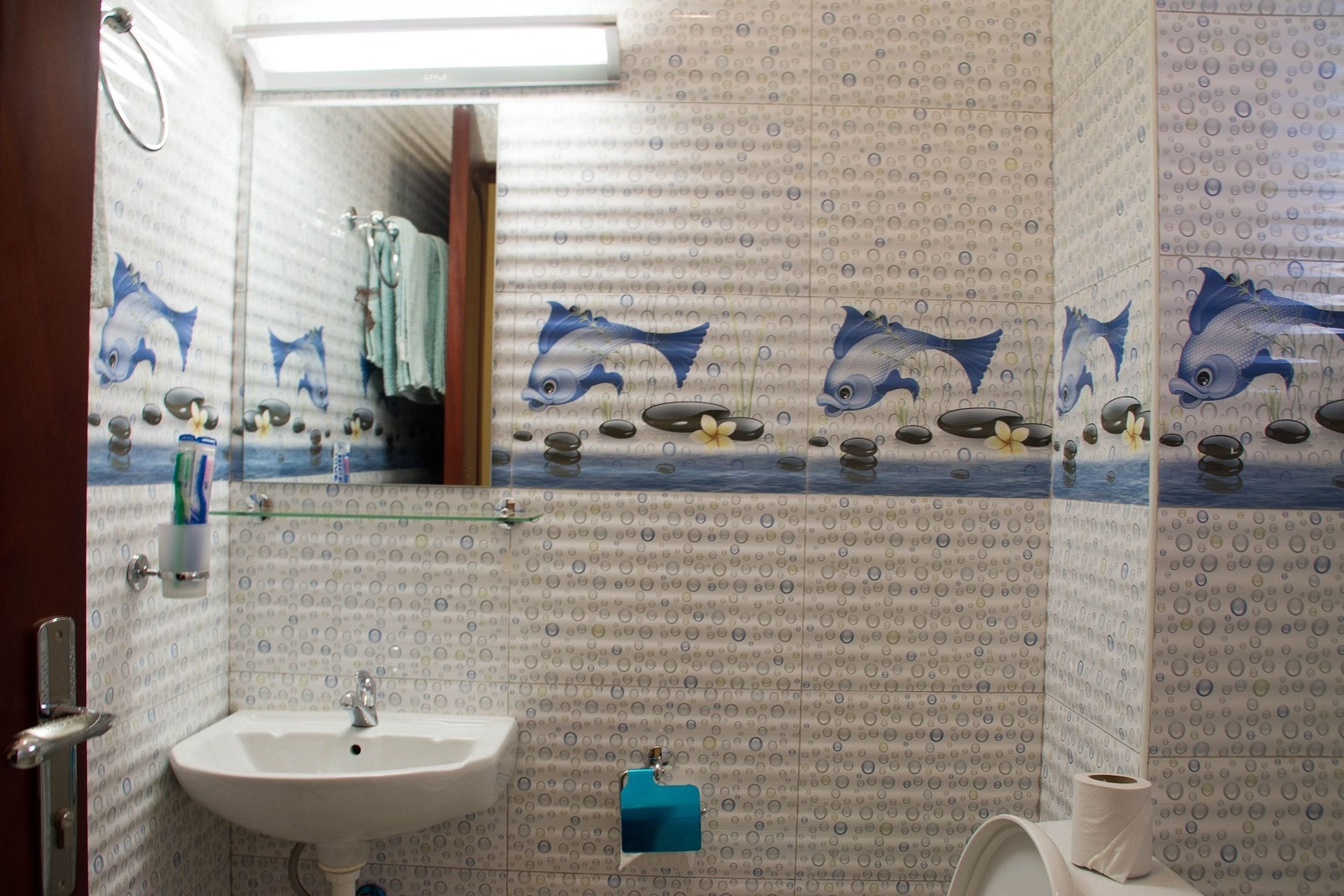 A bathroom with a sink, mirror, and toilet. The walls have a pattern of circles and fish illustrations.