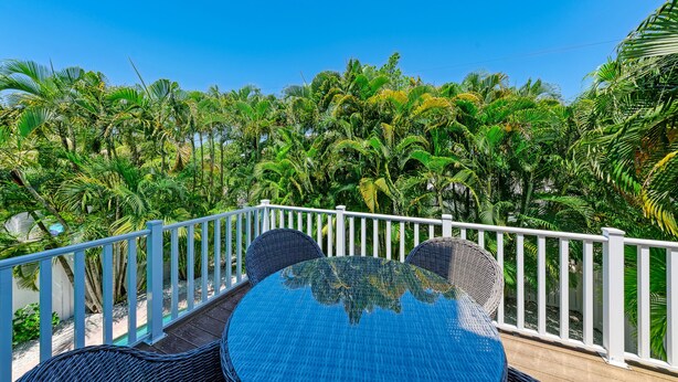 A balcony with a round table and two chairs, surrounded by a white railing, overlooking a lush tropical garden.