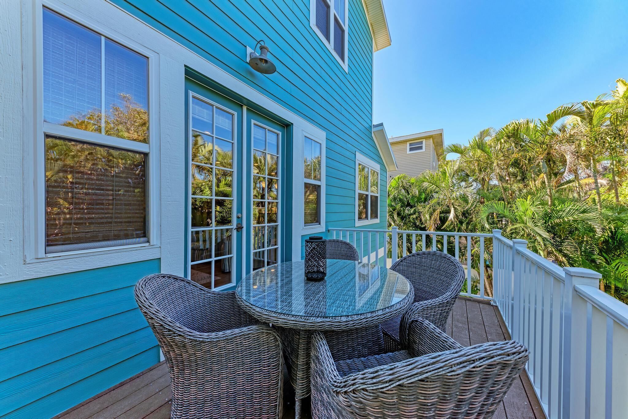 A blue house with a deck featuring wicker furniture and a glass table.
