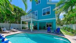 A two-story blue house with a pool, outdoor seating, and a fenced backyard.