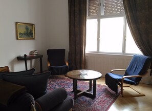 A living room with a sofa, two chairs, a small table, a painting on the wall, and a window with curtains.