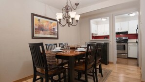 A dining area with a wooden table and chairs, a chandelier, and a kitchen in the background. - JHRL - Tensleep A2 - First floor condominium located in Teton Village (Teton Village)