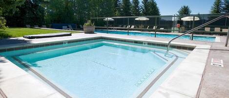 Piscina rectangular con borde de azulejos, rodeada de sillas de descanso y sombrillas, con un fondo de árboles.