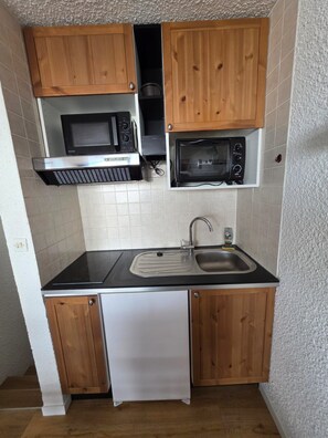 A compact kitchen with wooden cabinets, a microwave, a toaster, and a sink. - Starting with your skis from the residence. 
On the slopes - Full sun -Brelin (Les Belleville)