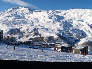A snow-covered mountain with ski slopes, buildings, and a clear sky.