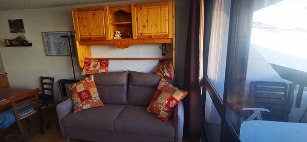 A cozy interior with a sofa, wooden cabinets, a dining table, and a window with a view.