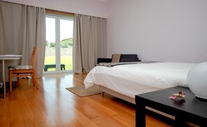 A bedroom with a bed, a desk, a chair, and a view of a garden through a sliding door. - Martin Guest House AZORES (Terceira Island) Dream destination (PRAIA DA VITORIA)