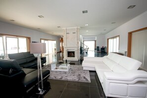 A modern living room with a fireplace, black and white sofas, and a glass coffee table. - Martin Guest House AZORES (Terceira Island) Dream destination (PRAIA DA VITORIA)