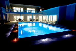 A swimming pool with lounge chairs and a covered seating area, surrounded by a two-story building with large windows. - Martin Guest House AZORES (Terceira Island) Dream destination (PRAIA DA VITORIA)