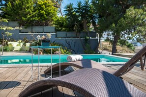 Un espace aménagé au bord de la piscine, avec des fauteuils de relaxation en osier, une petite table ornée d’un vase de fleurs et une vue sur la piscine.