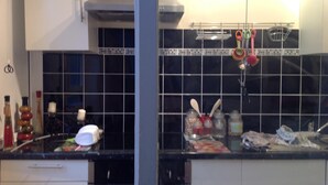 Cozinha com painel de azulejos pretos, eletrodomésticos de aço inoxidável e diversos utensílios de cozinha.