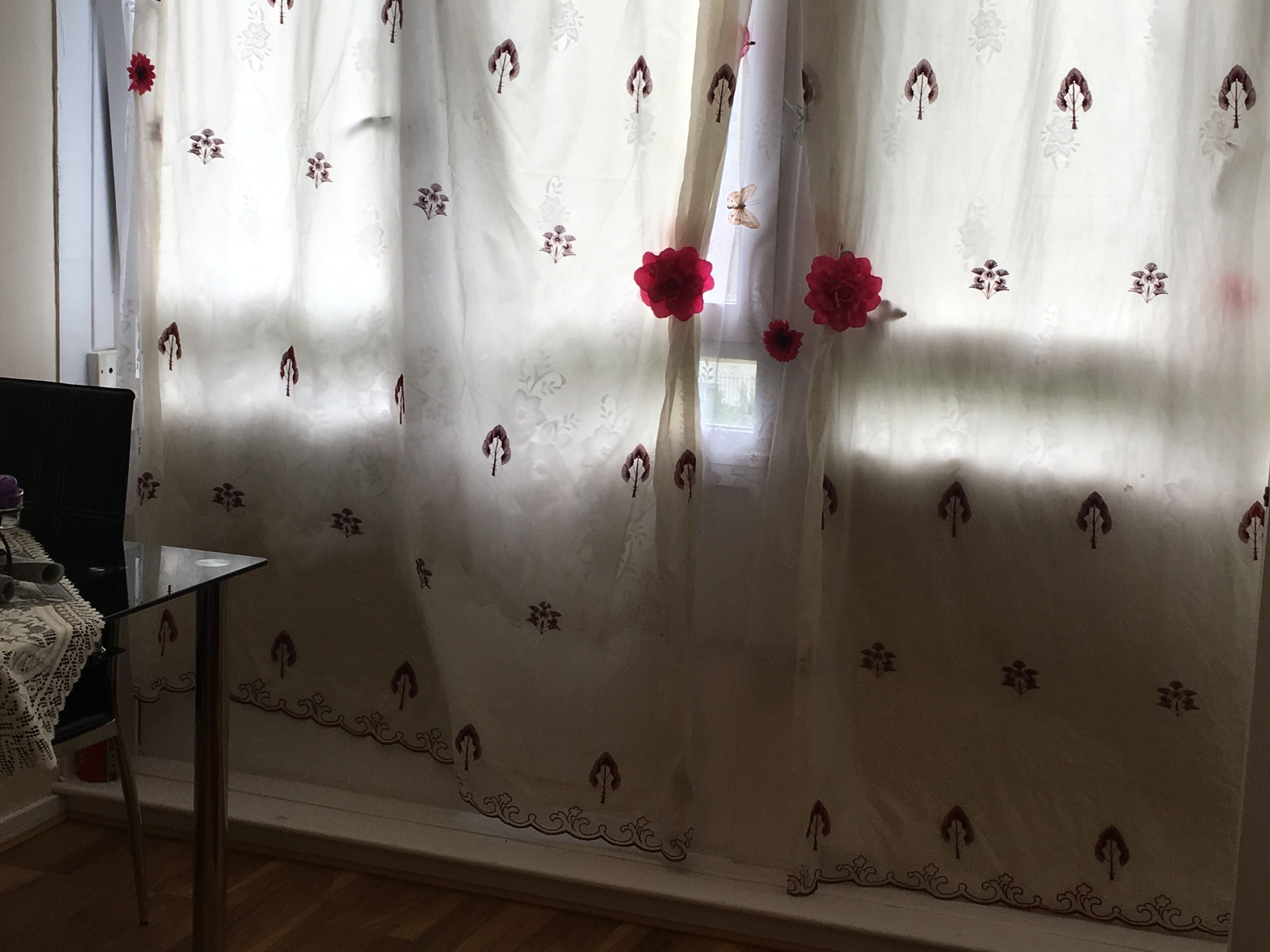 A room with a bed, a chair, and a window with sheer curtains featuring floral patterns.