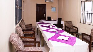 Un salón de conferencias con una larga mesa, sillas estampadas y un ventanal con barrotes.