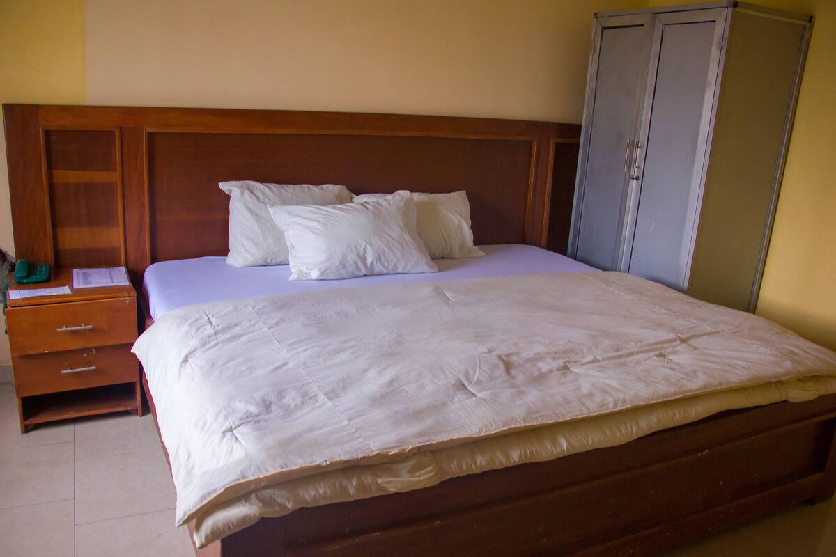 A neatly made bed with white linens and pillows, a wooden headboard, a wooden nightstand with drawers, and a wardrobe.