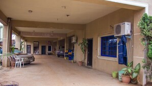 A covered outdoor area with a car parked under a shelter, potted plants, and a blue window. - Emota Paradise Phase 2 (Lagos)