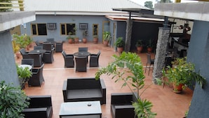 An outdoor patio area with multiple tables and chairs, surrounded by potted plants. - Kings Celia Hotel & Suites (Lagos)