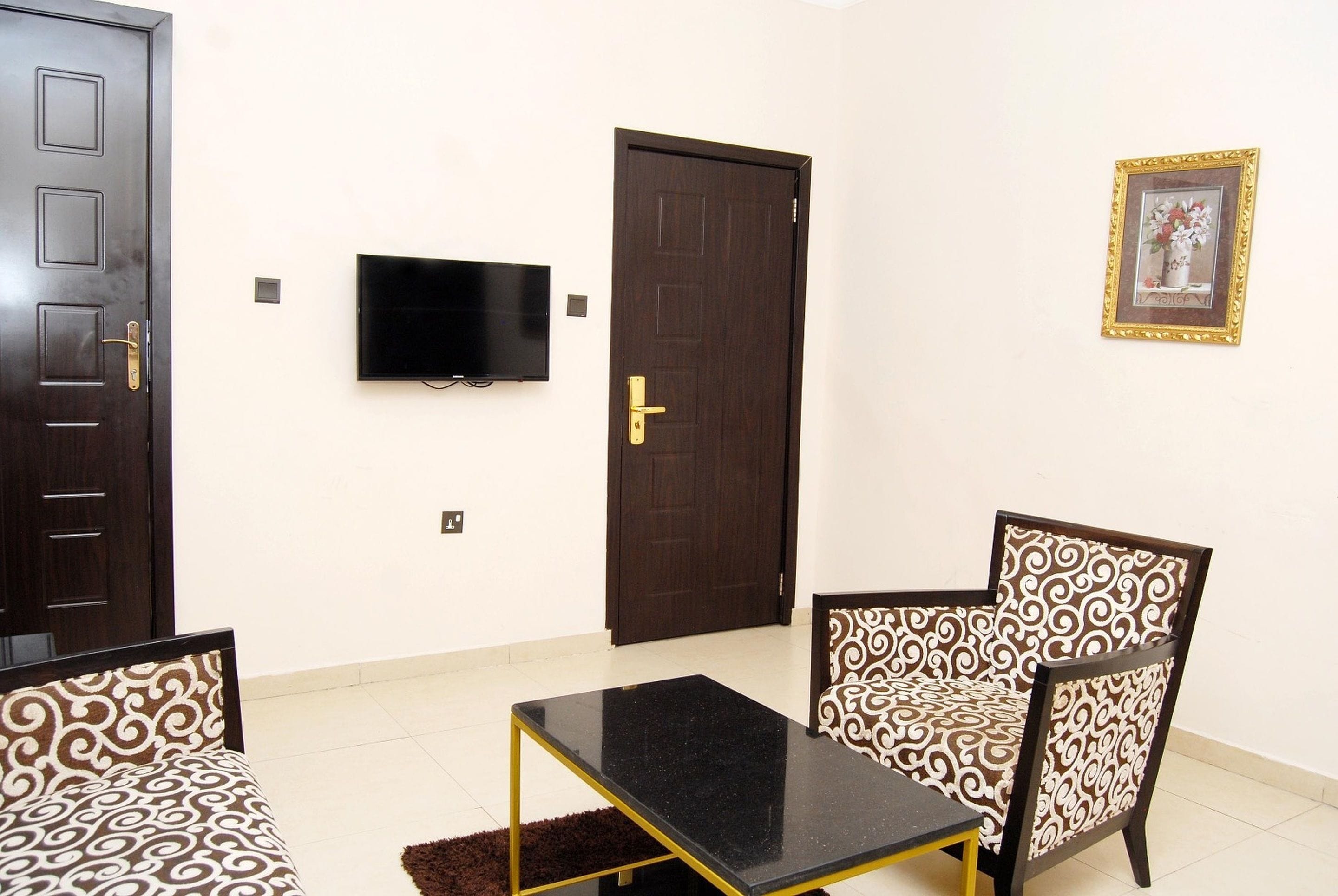 A room with a sofa, a coffee table, a patterned chair, a television, and a door.