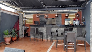 An outdoor bar area with a stone wall, bar stools, and potted plants. - Kings Celia Hotel & Suites (Lagos)